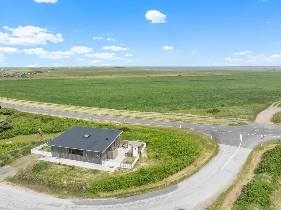 A small modern building sits beside a rural road, surrounded by open fields.