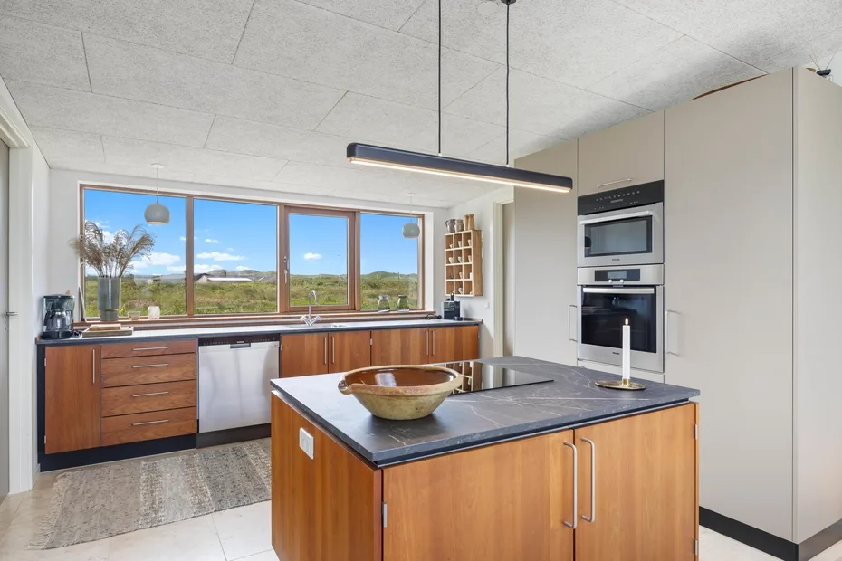 A modern kitchen with wooden cabinetry, a central island, and wide windows.
