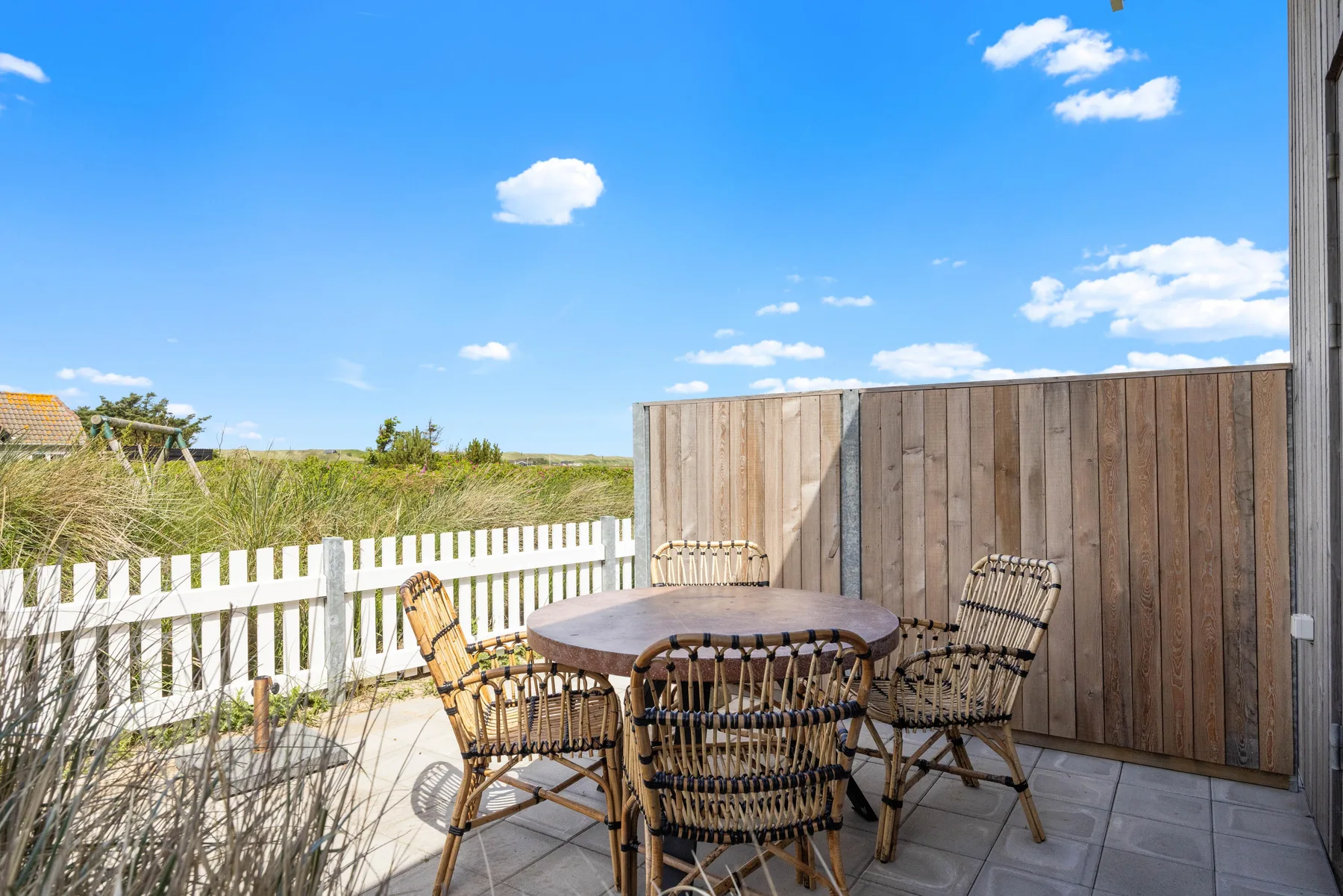 An outdoor patio with a table and seating beside a wooden privacy screen.