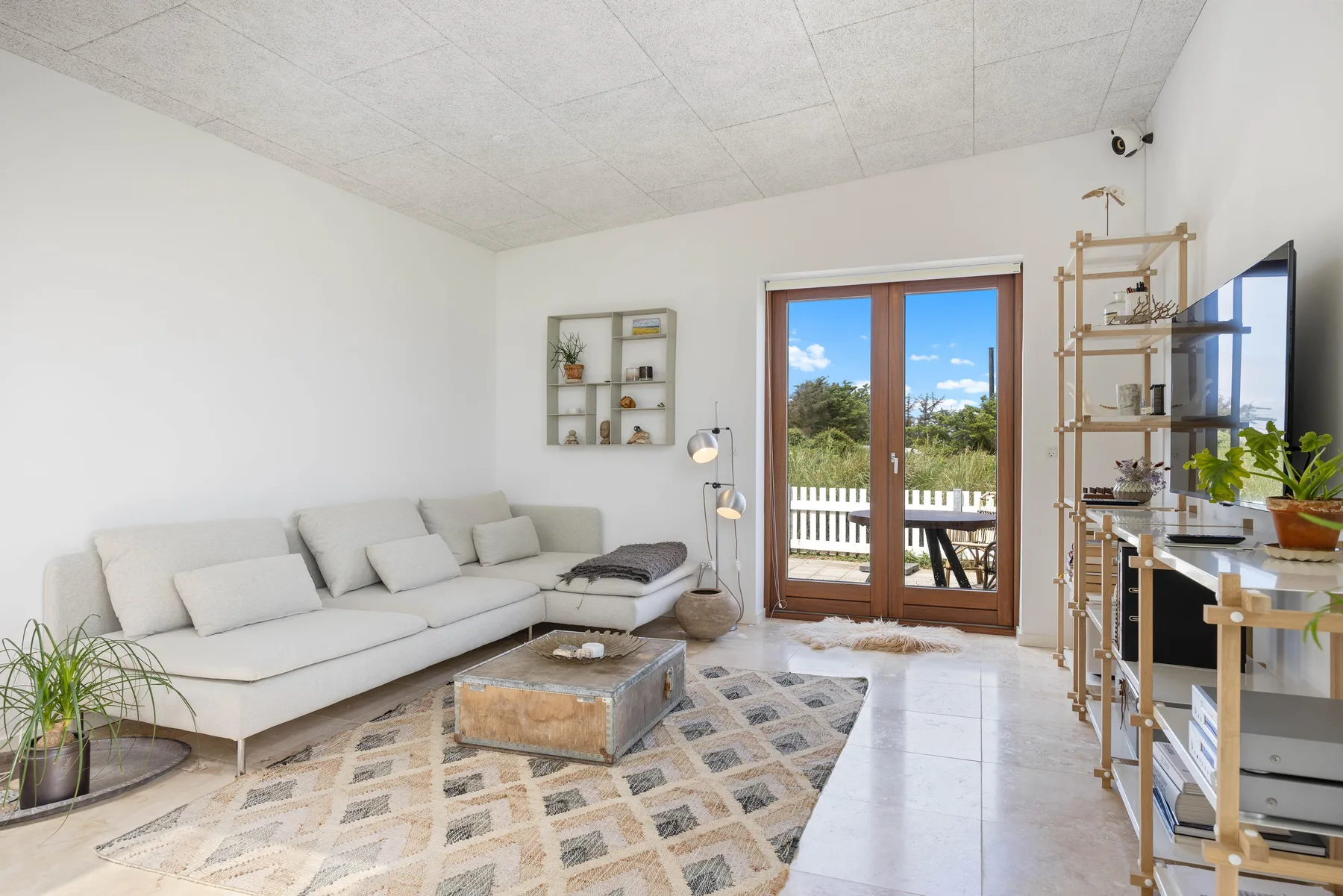 A bright living room with seating, a patterned rug, and glass doors opening onto a deck.