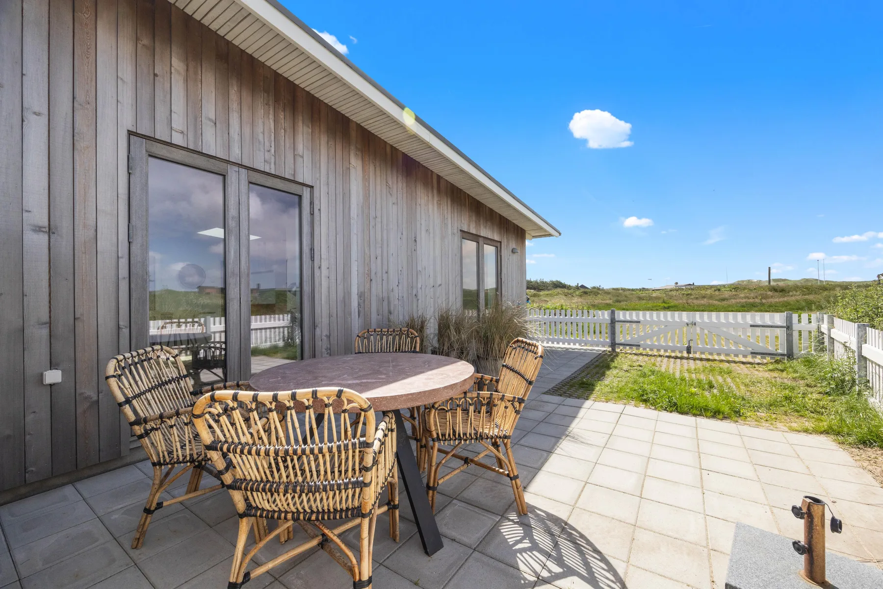 A patio beside a wooden-sided house has a table and woven seating.