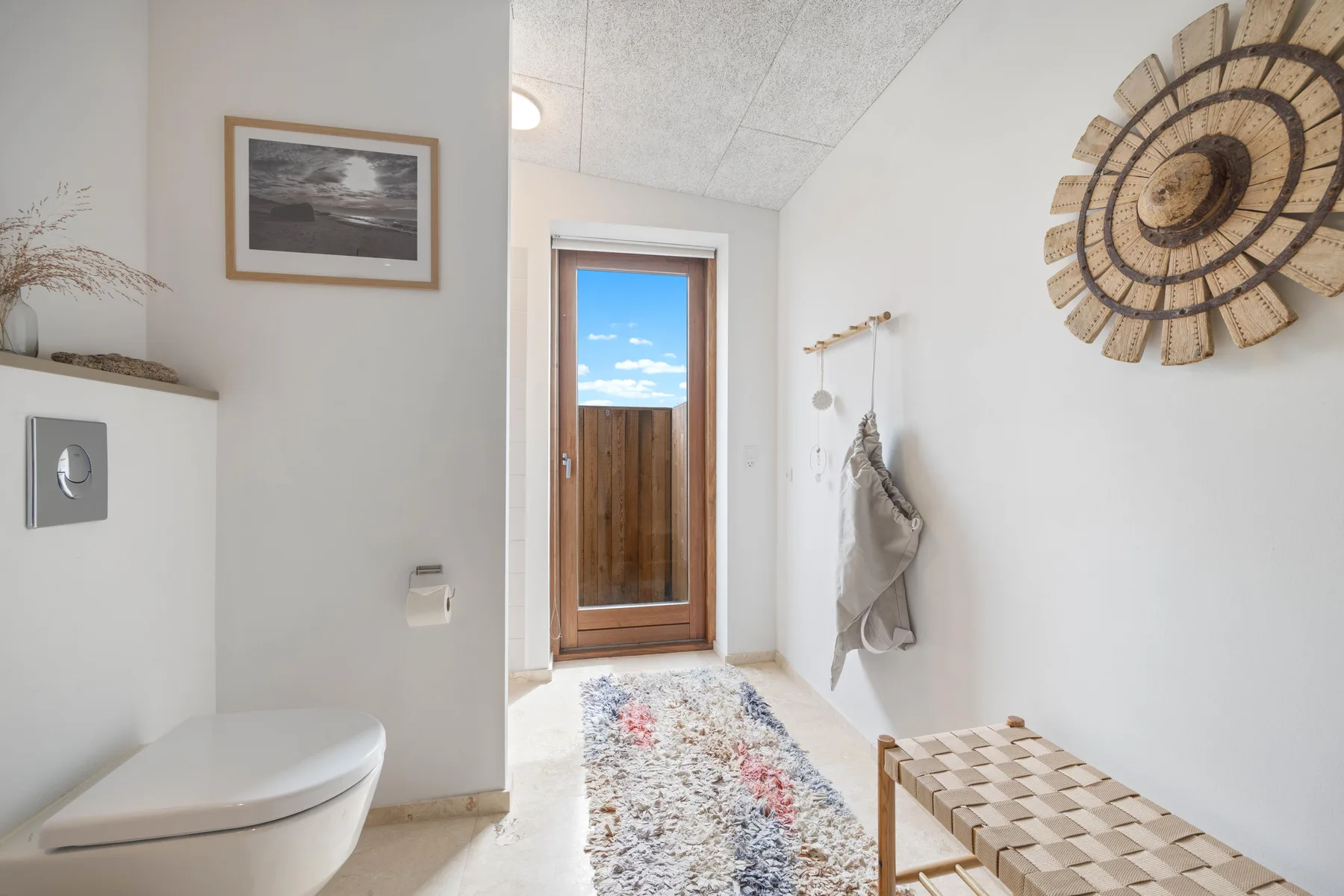 A bright bathroom with a toilet, patterned rug, and wooden door.