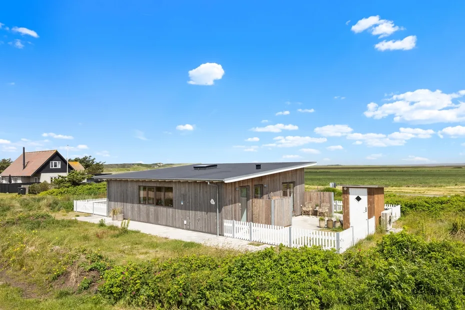 A low modern building stands amid green vegetation beneath a wide blue sky.