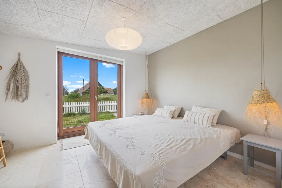 A bright bedroom with a large bed beside glass doors opening onto a balcony.