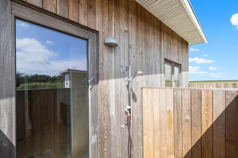 An outdoor shower beside a wooden exterior wall and privacy screen.
