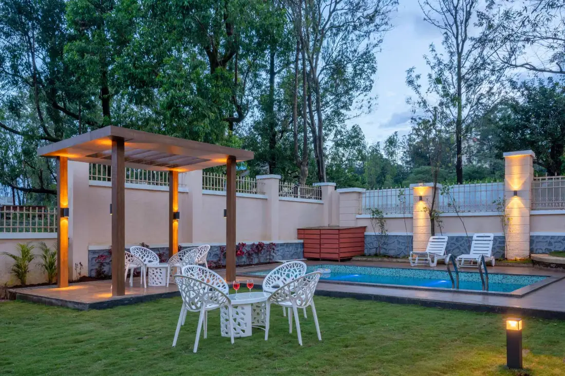 Zona exterior junto a una piscina, con pérgola, césped y árboles alrededor.