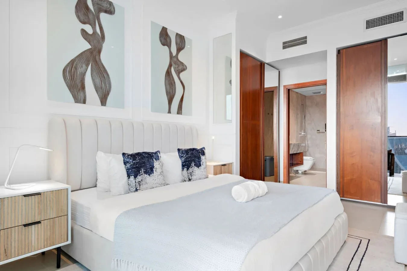 A bright bedroom with a neatly made bed and abstract artwork above the headboard.