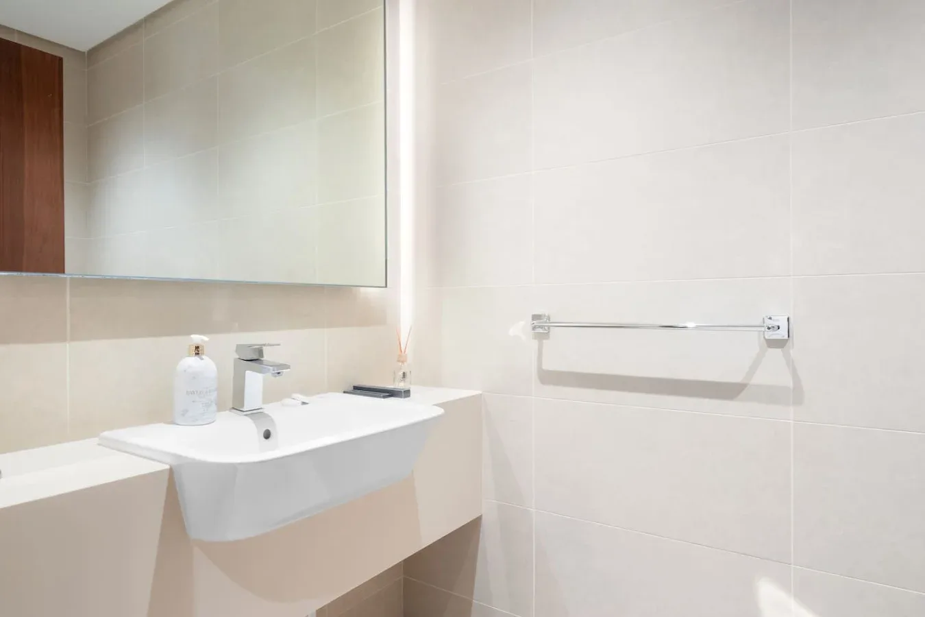 A tiled bathroom with a wall-mounted sink and a large mirror.