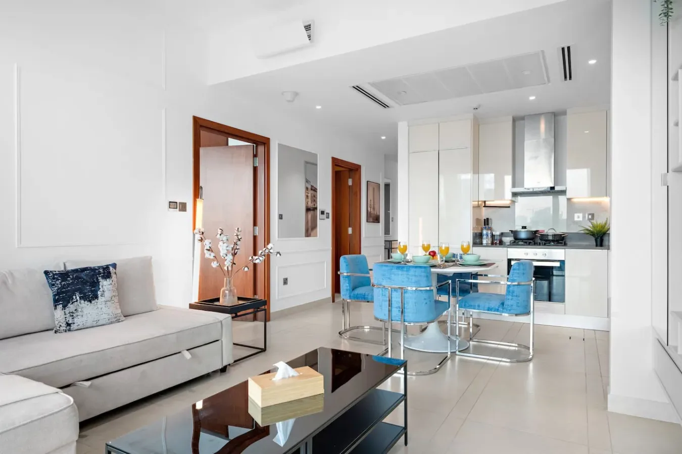 A bright living and dining area opens onto a kitchen, with blue seating around the table.