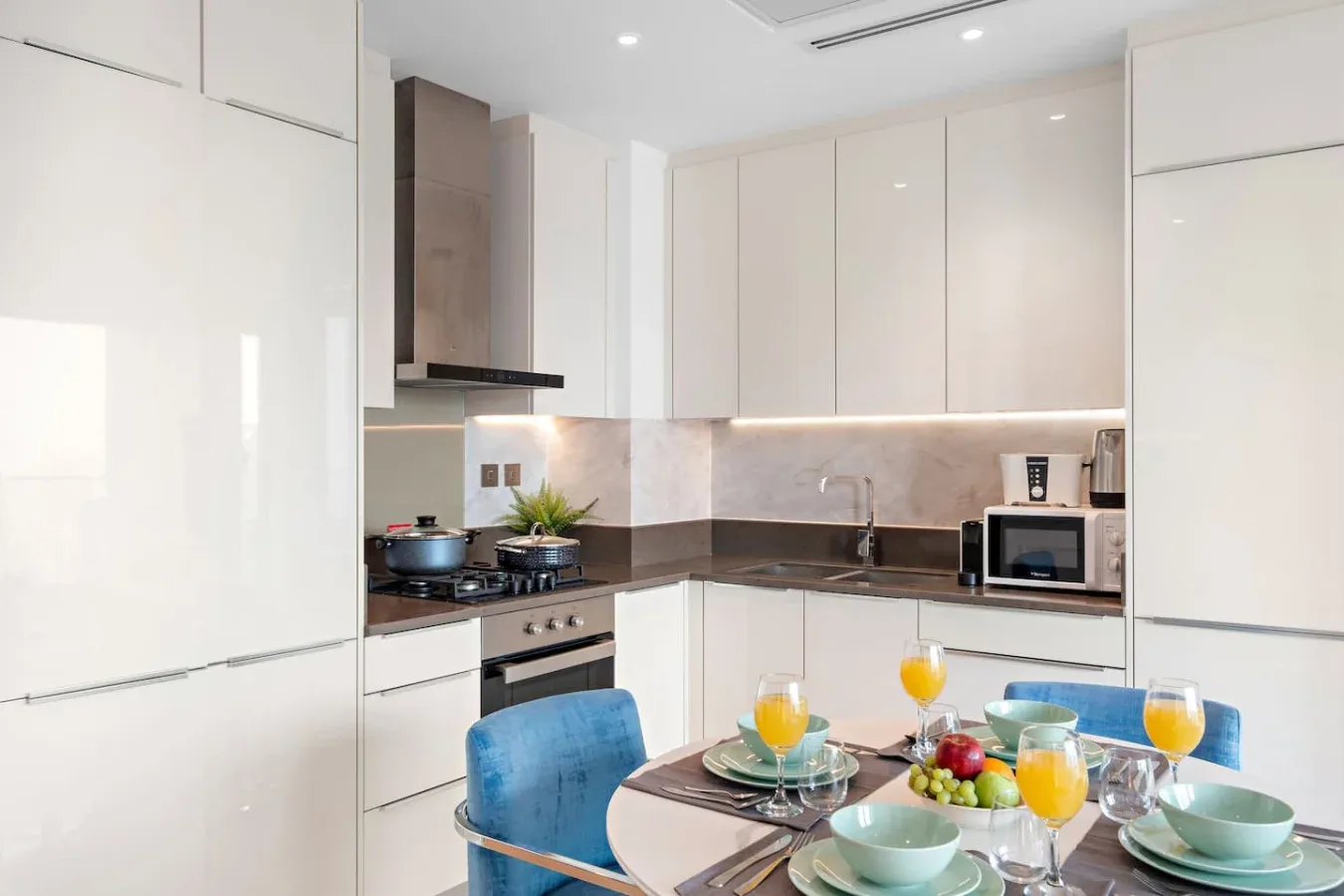 A bright modern kitchen with white cabinets and a dining table set with dishes and fruit.