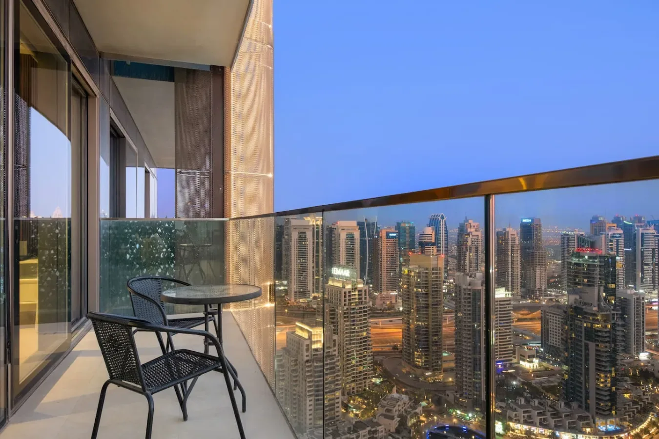 A balcony with seating overlooks a city skyline at dusk.