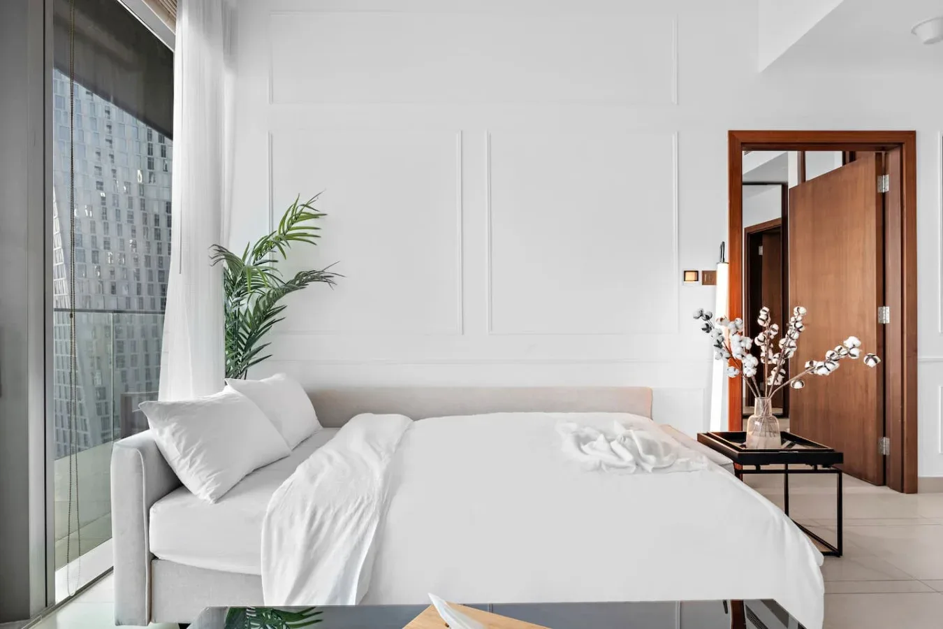 A bright bedroom with a white bed beside a large window.