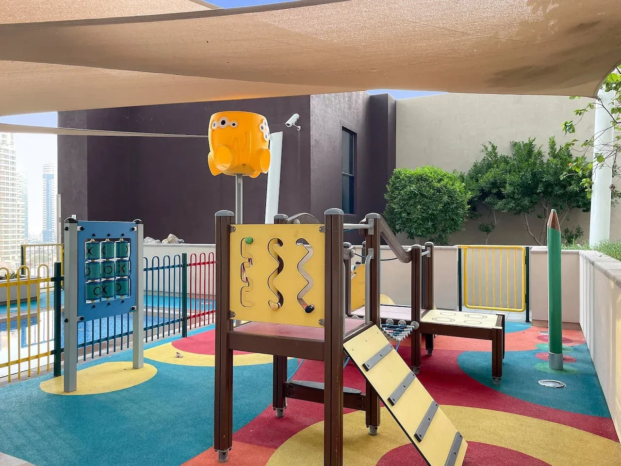 A colorful outdoor playground with climbing panels and play equipment under a shade canopy.
