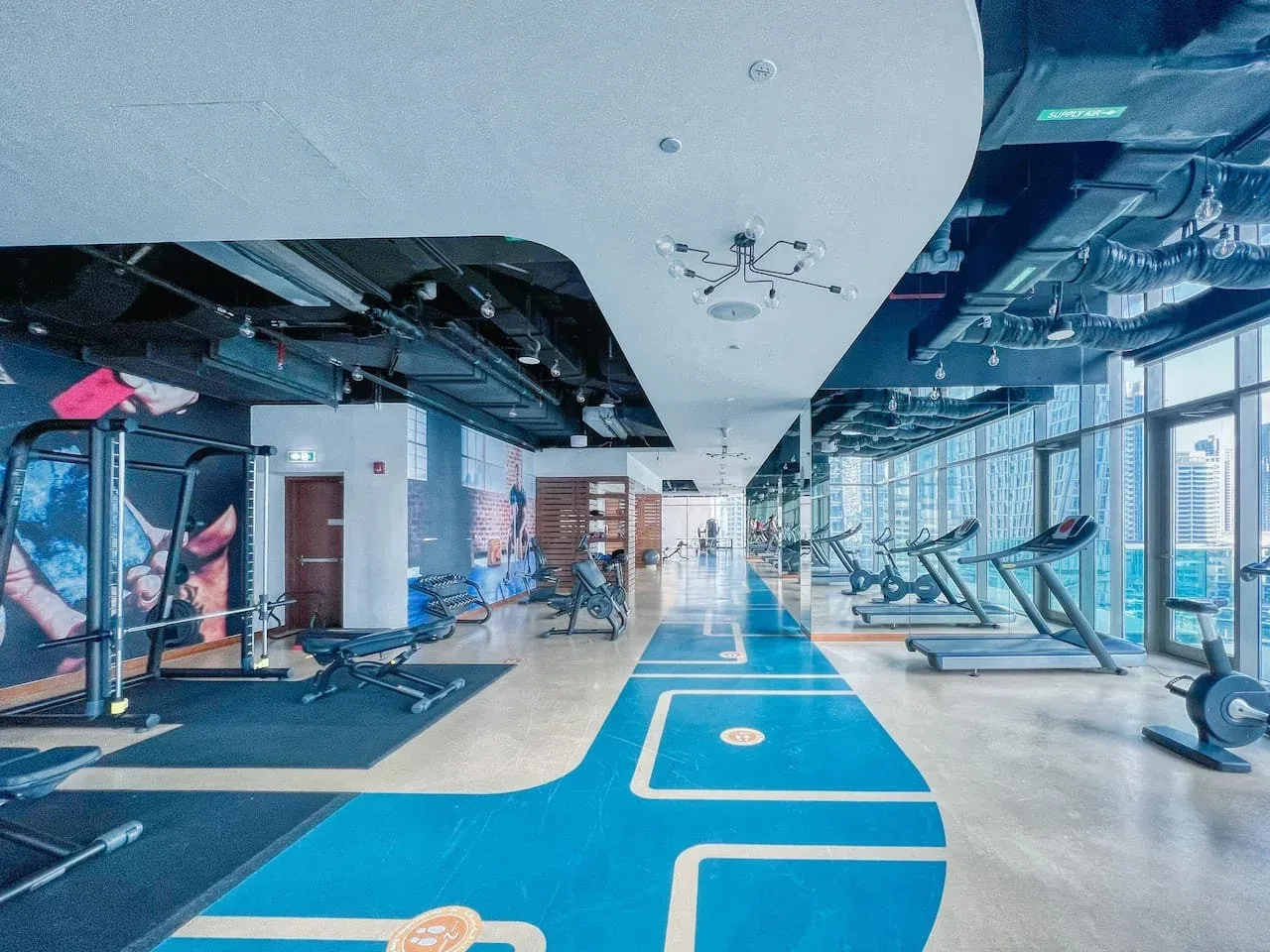 A gym with treadmills and weight-training equipment beside a blue exercise floor.