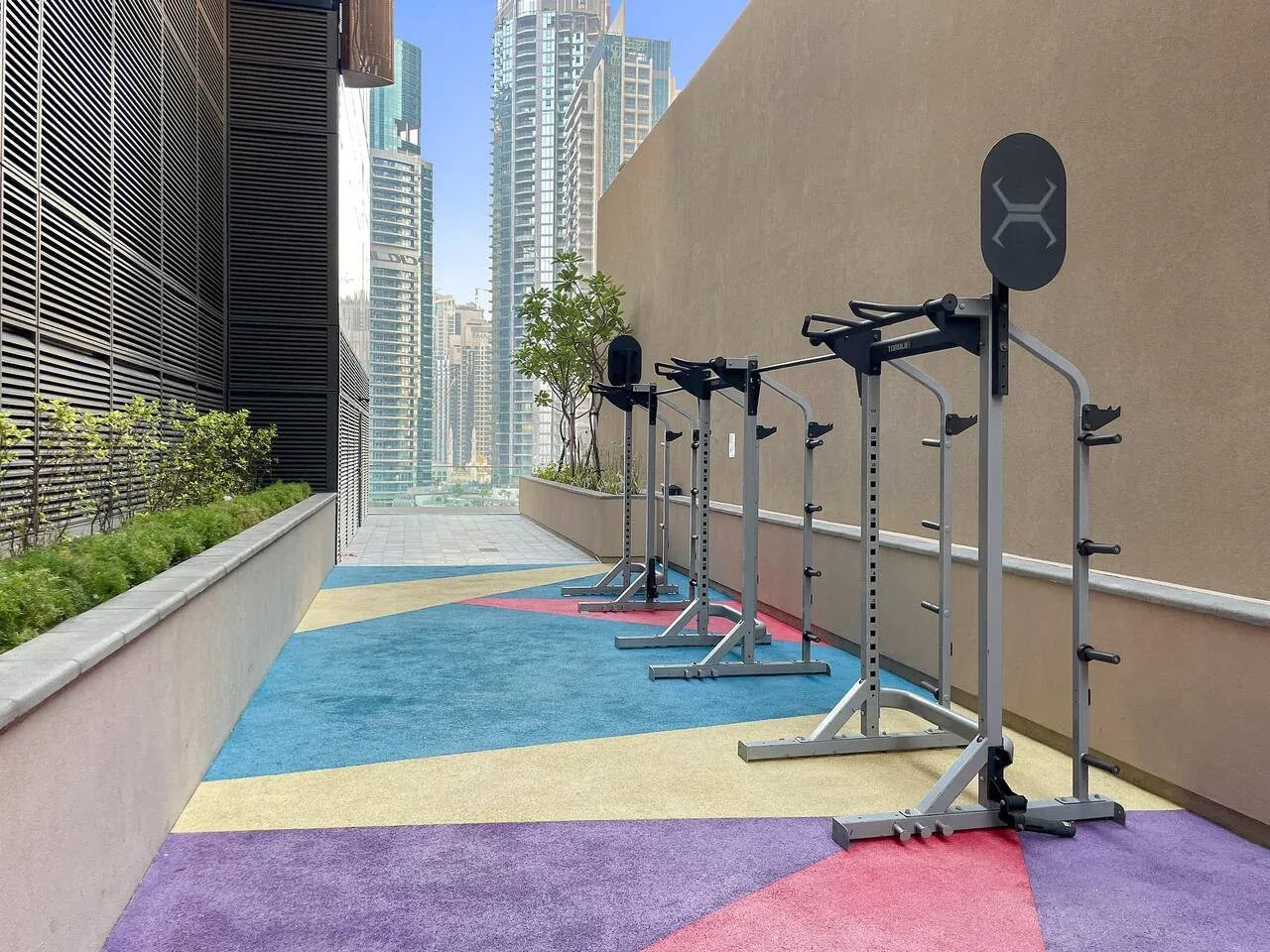 An outdoor exercise area has fitness stations arranged along a brightly colored walkway.