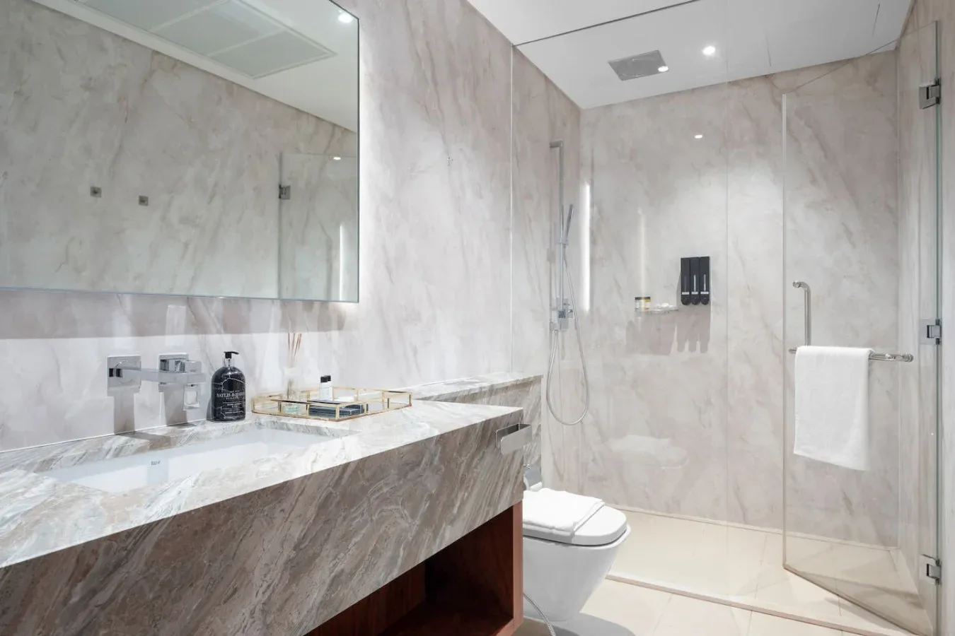 A bright marble bathroom with a wide vanity, mirror, and glass shower.