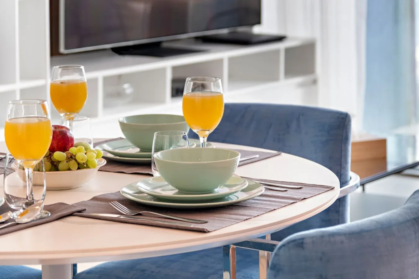 A dining table set with dishes, fruit, and glasses of orange juice.