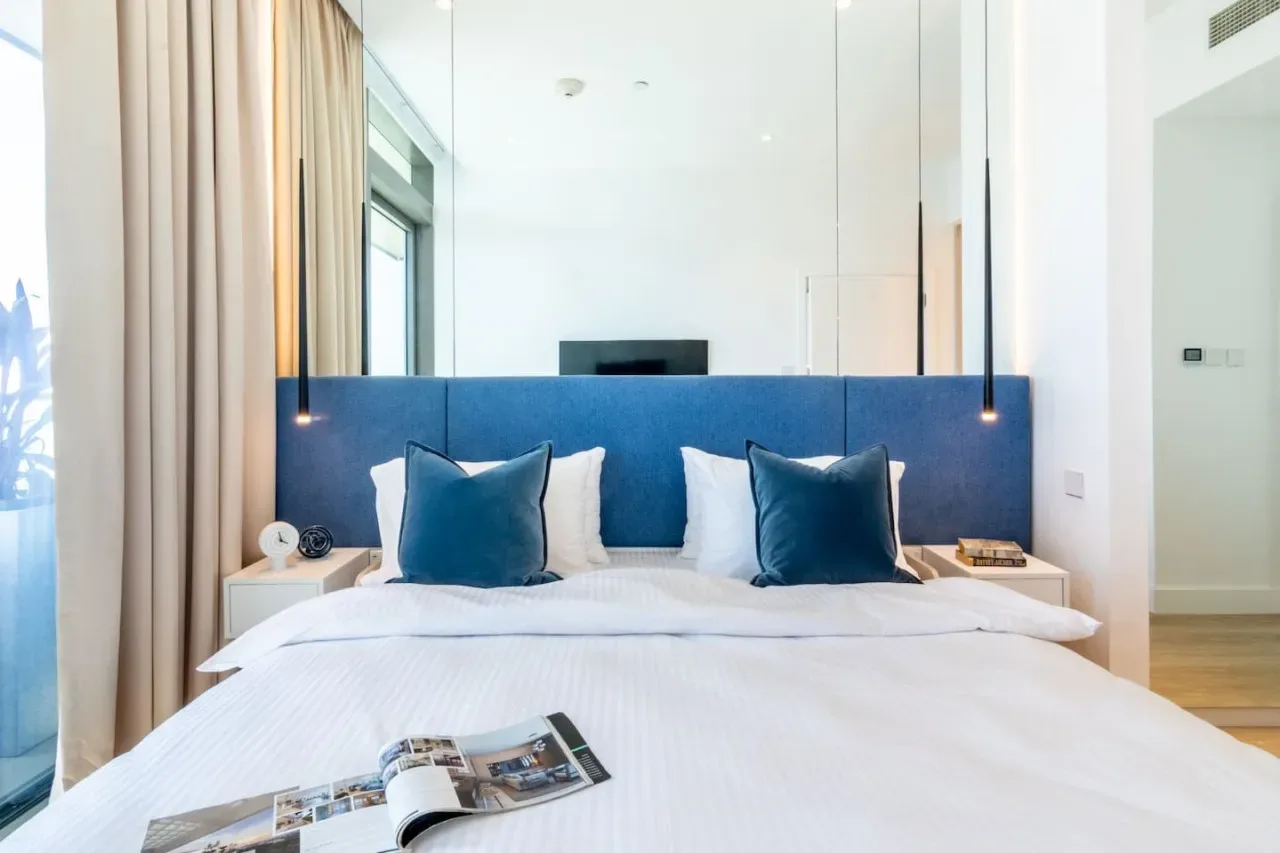 Un dormitorio luminoso con una cama tendida y cojines azules.