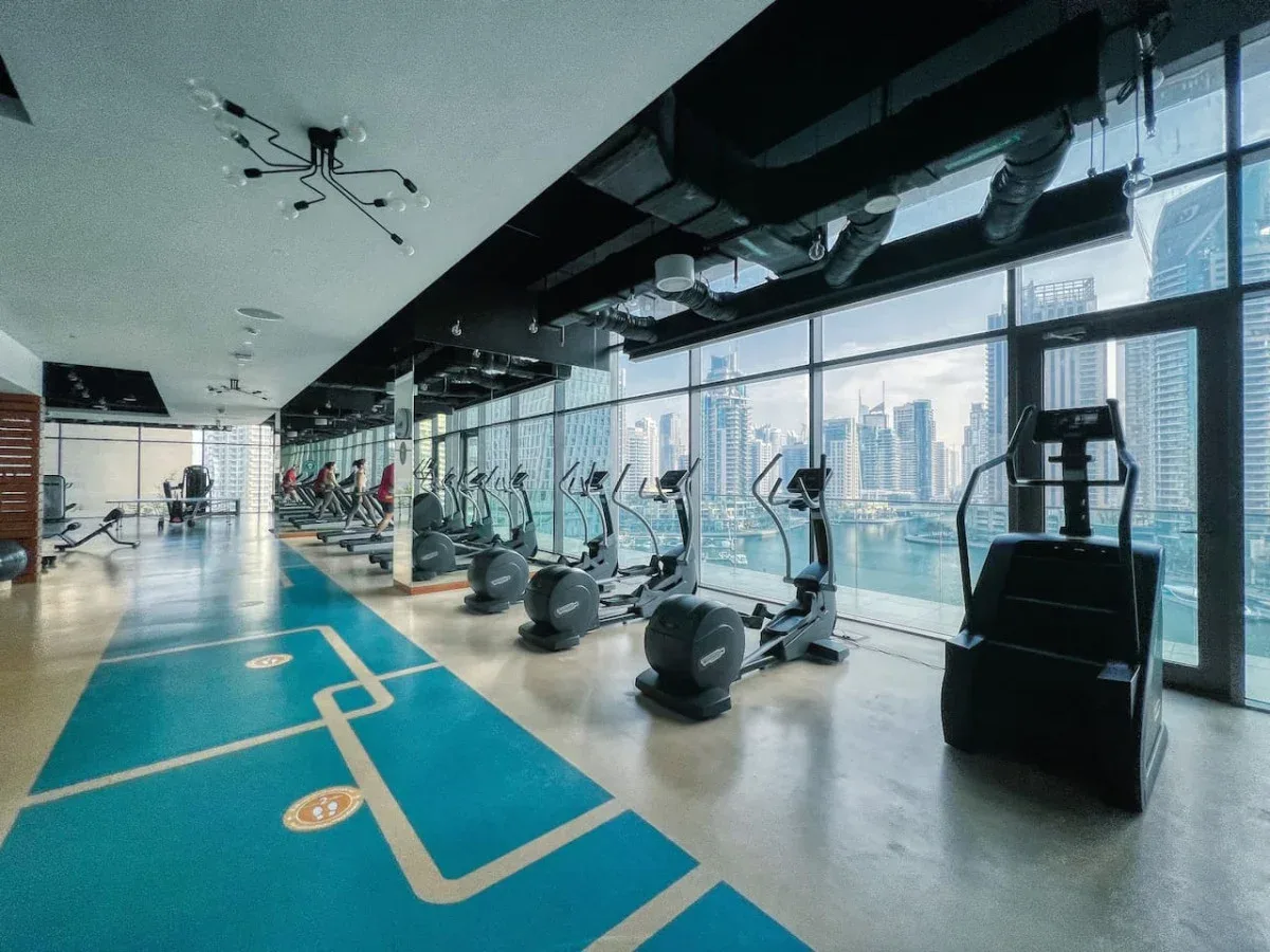Un gimnasio con máquinas de ejercicio junto a ventanales con vistas a la ciudad.