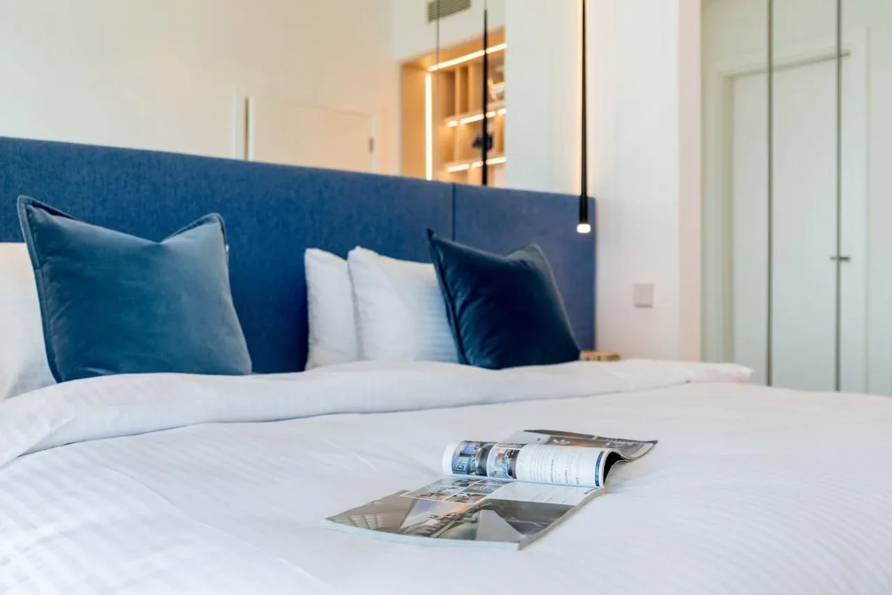 Una cama bien tendida con almohadas azules y una revista.