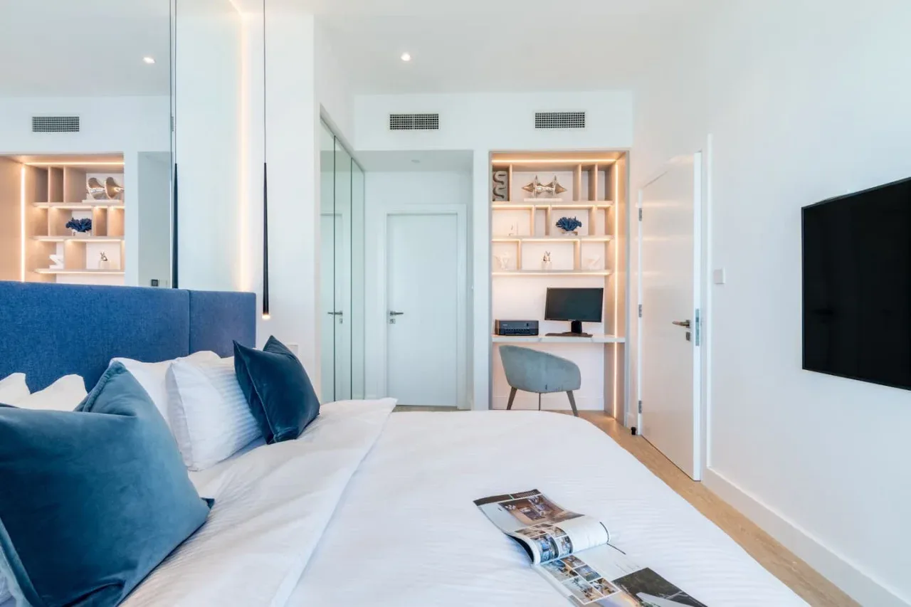 Un dormitorio luminoso con una cama, estanterías empotradas y un escritorio.