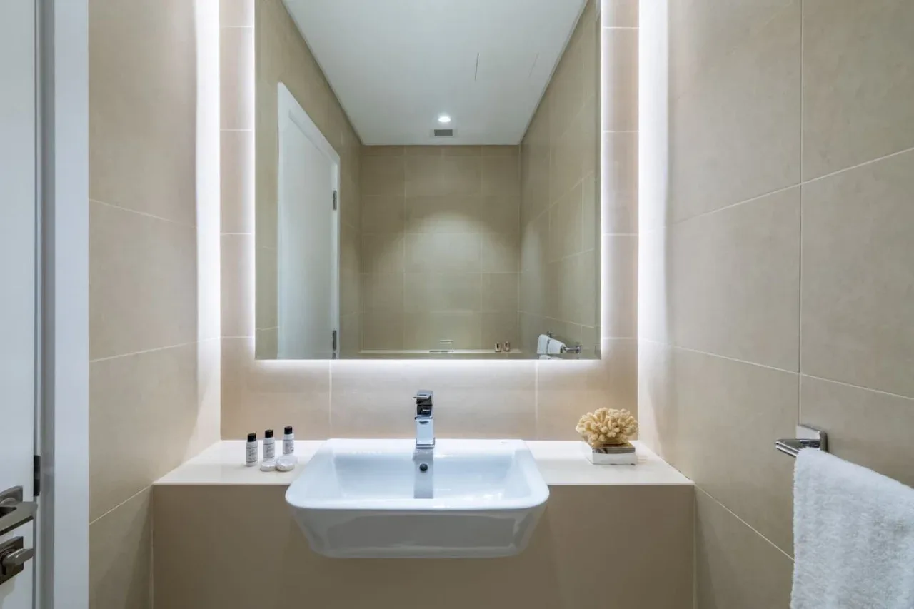 Un lavabo de baño se encuentra bajo un amplio espejo iluminado.
