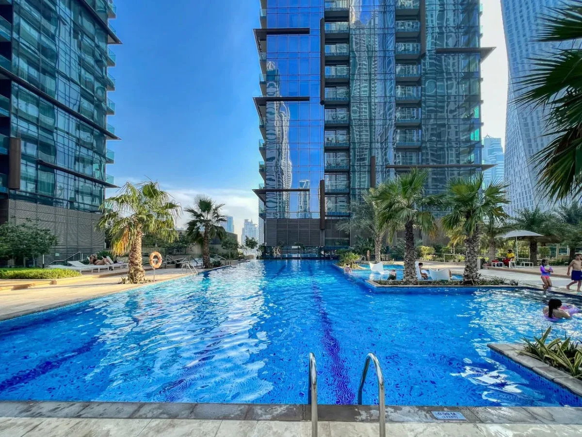 Una piscina se encuentra entre edificios altos modernos, con palmeras junto a la zona de descanso.