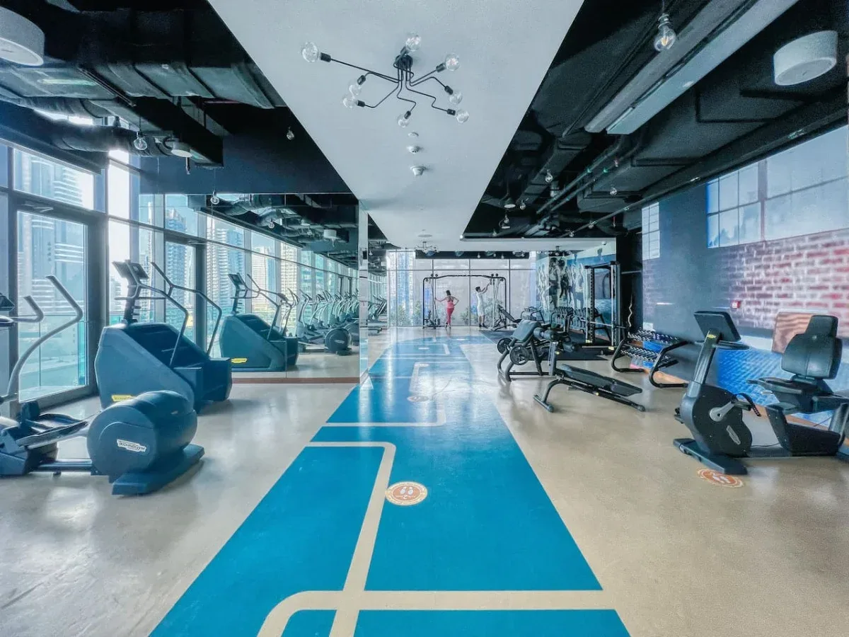 Un gimnasio luminoso con máquinas de ejercicio, marcas azules en el suelo y paredes con espejos.