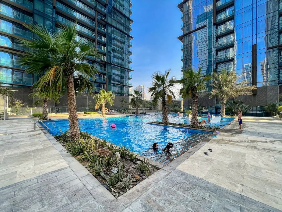 Una piscina al aire libre está rodeada de palmeras y edificios altos de cristal.