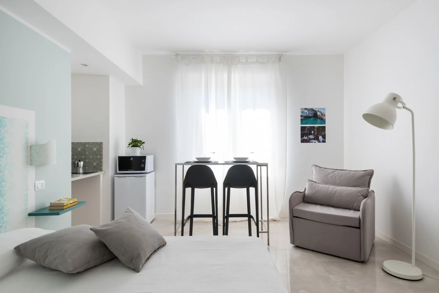 Un estudio luminoso tiene una cama, una mesa pequeña y un sillón.