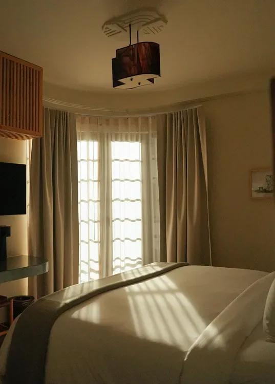 Bedroom with a bed, curtained window and wooden lamp.