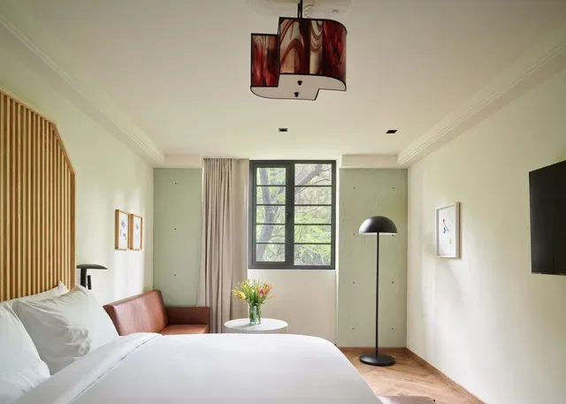 Hotel room with a bed, sofa, window and patterned lampshade.
