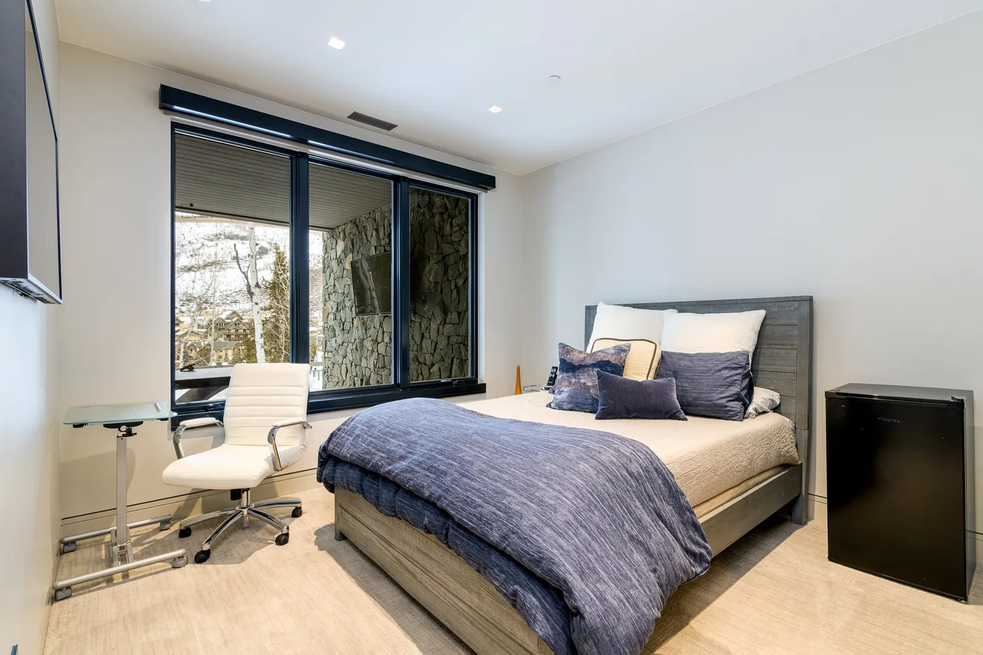 A bedroom with a bed, desk chair, and large windows.