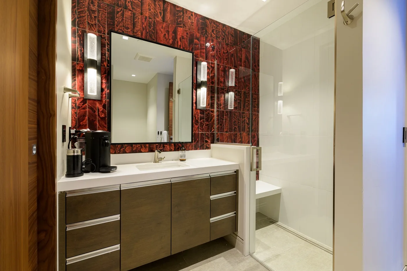 A bathroom vanity with a large mirror sits beside a glass shower.