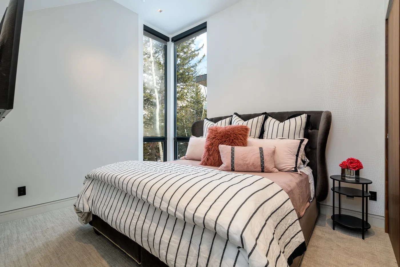 A bedroom with a striped bedspread, pink pillows, and tall corner windows.
