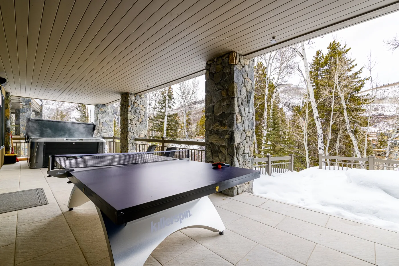 A covered patio features a ping-pong table beside a snowy outdoor view.