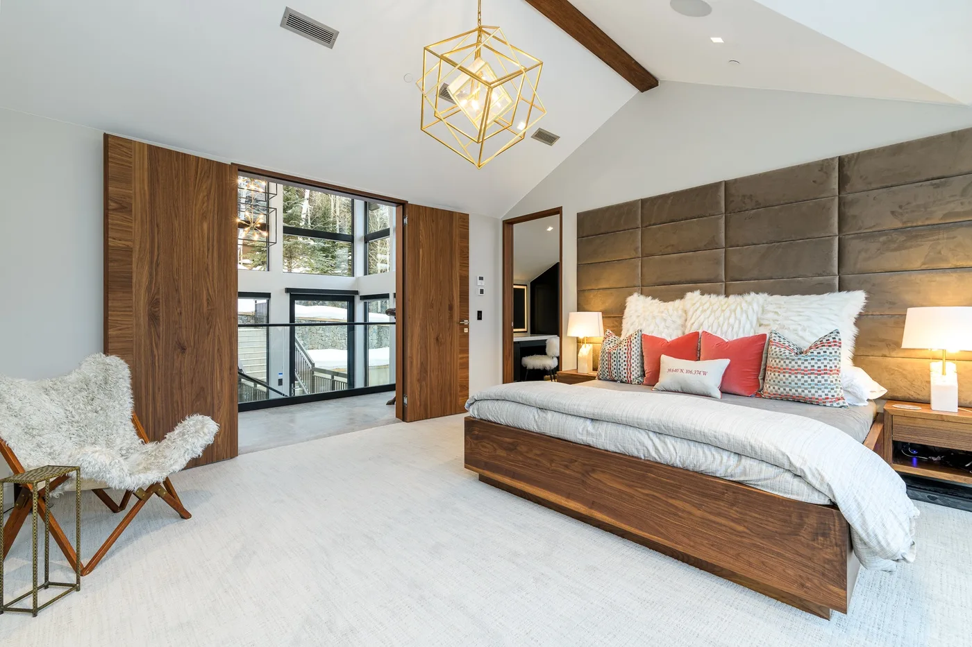 A bedroom with a large bed, padded headboard, and tall windows.
