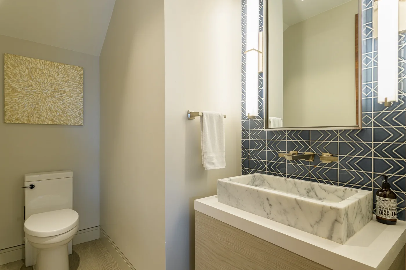 A bathroom features a marble vessel sink against a dark patterned tile wall.