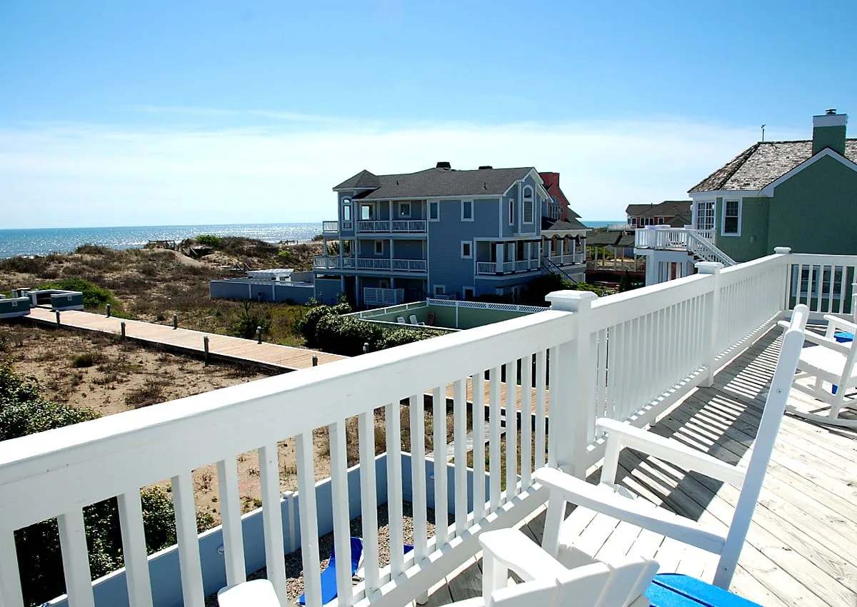 A white-railed seaside deck overlooks coastal homes and the ocean.
