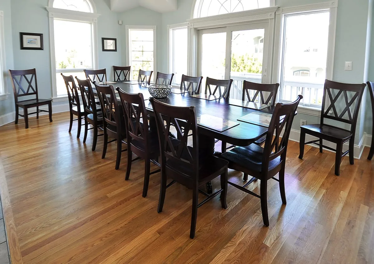 A bright dining room with a long table and dark wooden seating.