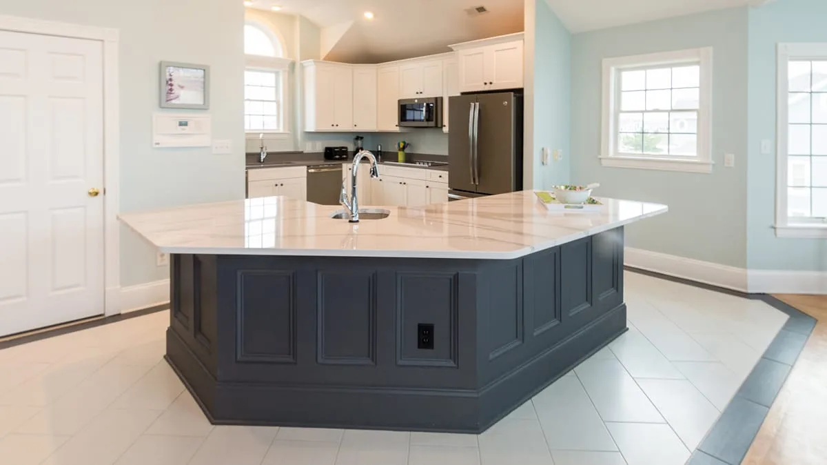 A bright kitchen with a large island, white cabinets, and stainless steel appliances.