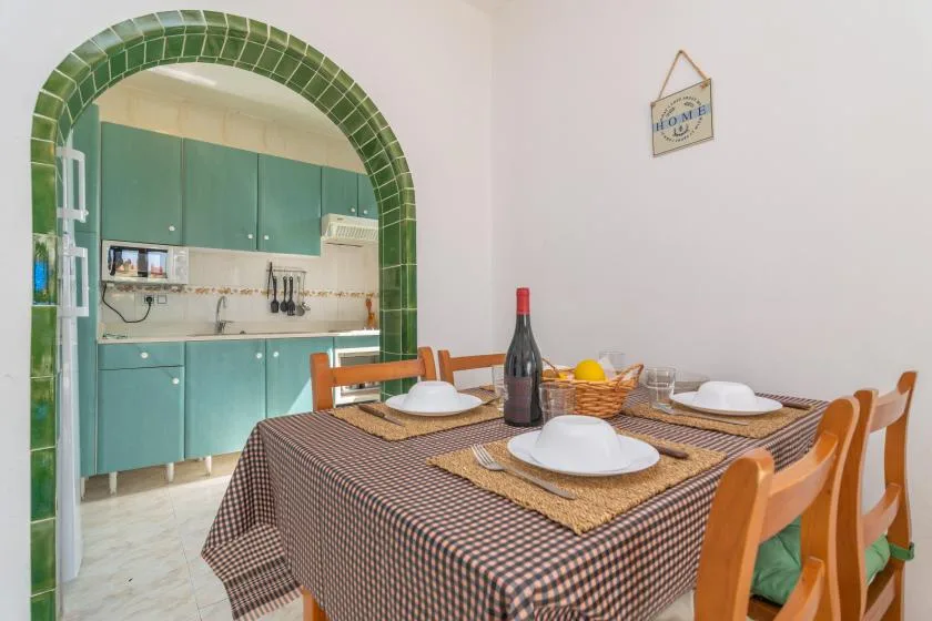 Una mesa de comedor con platos está junto a una cocina con gabinetes verde azulado.