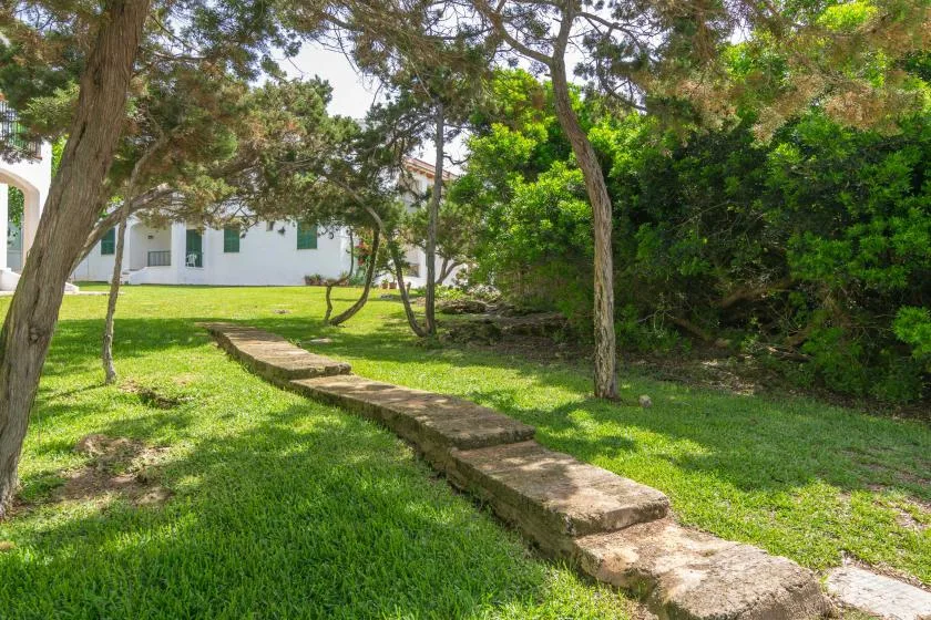 Un jardín de césped con árboles y un camino bajo de piedra junto a un edificio blanco.