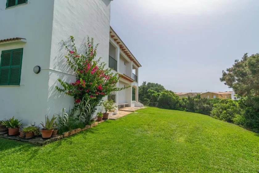 Una casa blanca está junto a un césped verde, con plantas floridas junto a la pared.