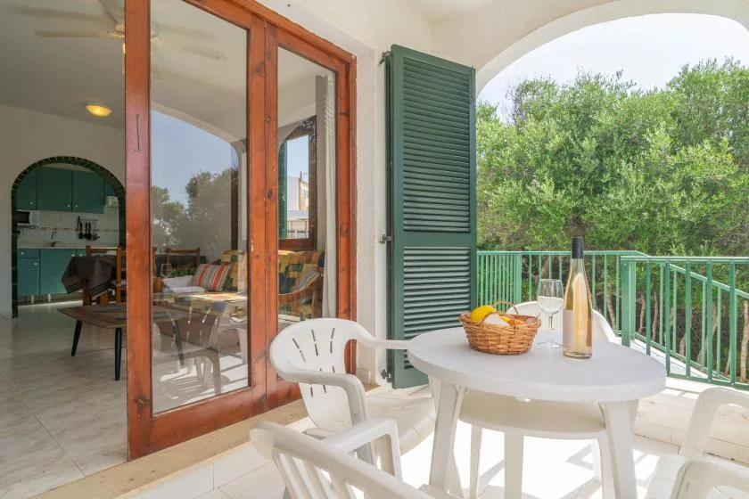 Una terraza soleada con una mesa redonda y sillas da a una zona verde.