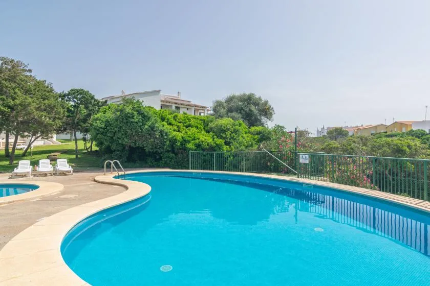 Una piscina exterior curva está rodeada de vegetación y asientos de descanso.
