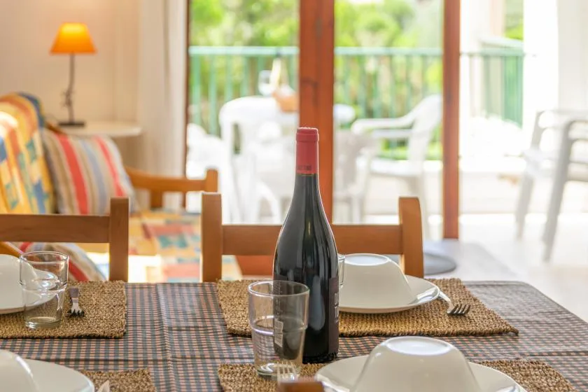 Una mesa está puesta con platos y vasos junto a una luminosa zona de estar.