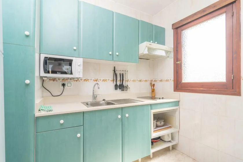 Una cocina luminosa con gabinetes turquesa, un fregadero y una ventana.