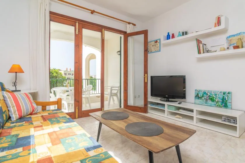 Una sala de estar con asientos coloridos, una mesa de centro y un televisor junto a puertas de vidrio.