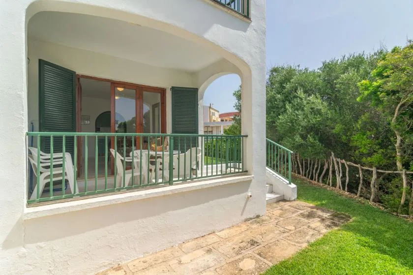 Una zona de estar exterior cubierta con barandilla verde da a un jardín.
